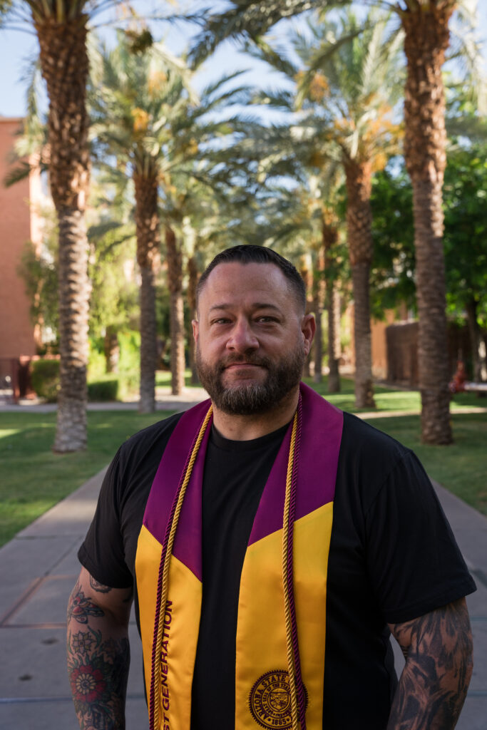 The photograph is a graduation portrait of John Rhorer, wearing a graduation stole and honor cords, at the ASU Palm Walk.