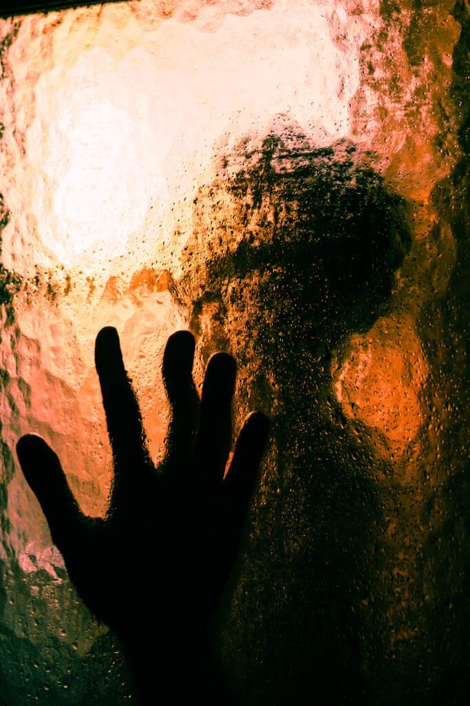 A picture of a woman behind a shower door focused on the beautiful light of the room. 