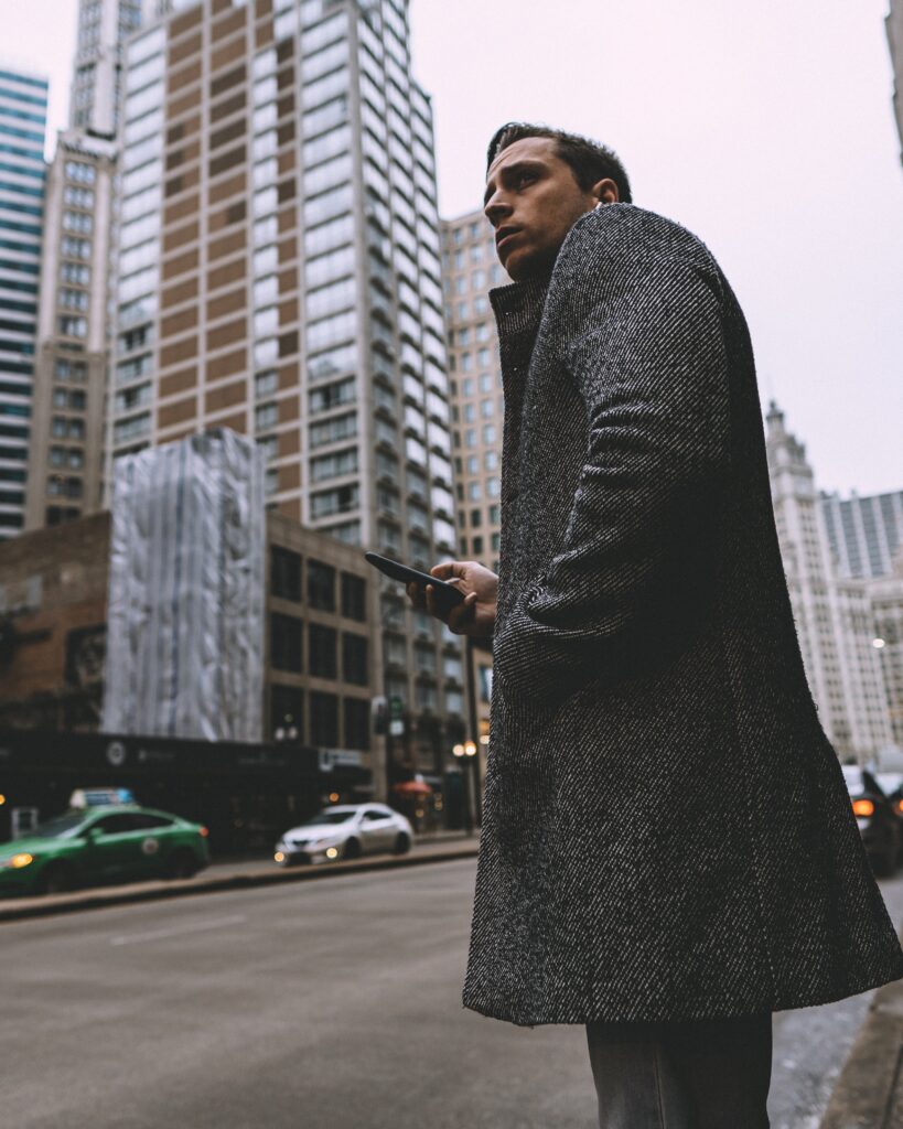 Street photo of a man in a trench coat in Chicago waiting for a taxi.